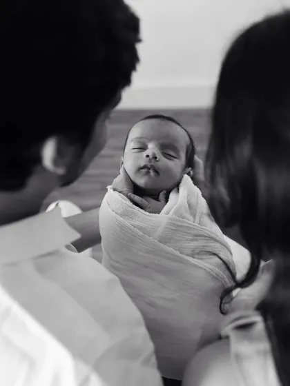 A black and white photo of parents looking down at their swaddled newborn. A beautiful, intimate moment.