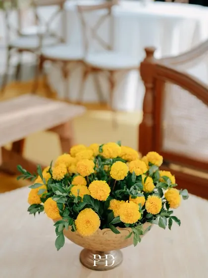 A close-up of the elegant seating area at a rooftop Haldi. The combination of traditional marigolds in brass bowls and modern, light-wood furniture creates a chic and sophisticated look.