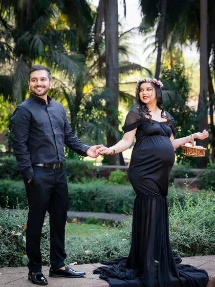 A stylish couple takes a stroll in the park. The mom-to-be looks elegant in a black gown and flower crown, holding a basket of flowers.