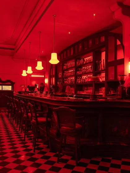 The bar at night, its checkerboard floor glowing under the red lights, creating a graphic and dynamic scene.