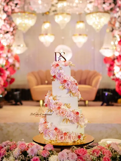A classic love story calls for a timelessly romantic cake. This five-tier wedding cake features a cascading spiral of handmade sugar flowers in soft pinks and whites, accented with delicate gold leaves for a touch of luxury.