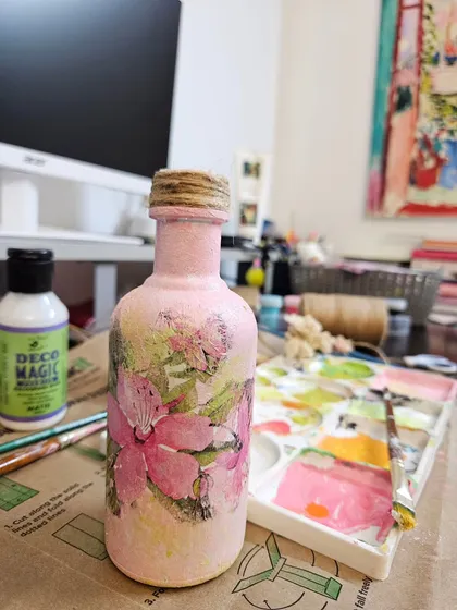 Here is a look at one of my one-of-a-kind decoupage pieces. I love transforming simple glass bottles into unique home decor items. This one features a soft pink texture and delicate floral motifs, perfect for a boho chic space.
