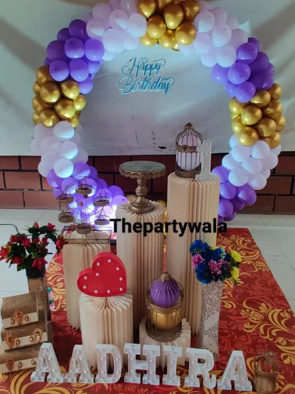 A purple, white, and gold balloon ring decoration. The setup includes vintage-style suitcases and a red heart prop for a unique touch.