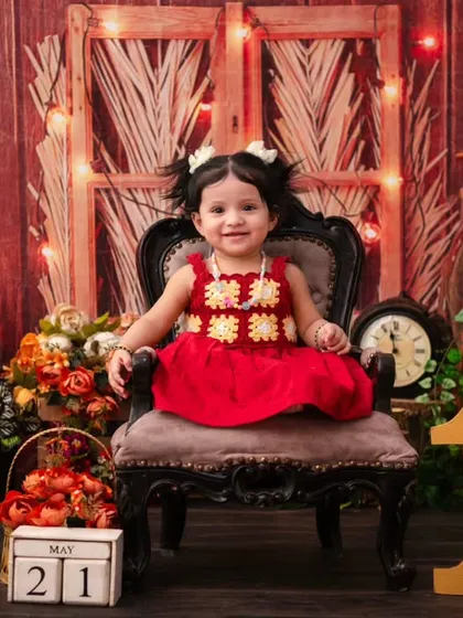 A rustic-themed first birthday shoot. The little girl in her red dress looks so charming sitting in the vintage-style chair, ready to celebrate turning one.