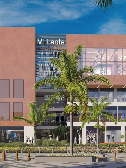 An exterior view of the V'lante scheme in Gurugram, a mixed-use development that combines retail with community spaces. The facade is designed for high visibility, with large glass windows and prominent signage.