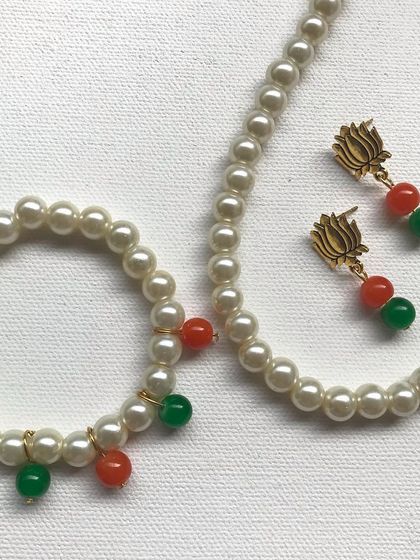 An elegant Independence Day jewellery set. It includes a pearl necklace and bracelet with saffron and green bead accents, plus matching earrings with a beautiful lotus stud.