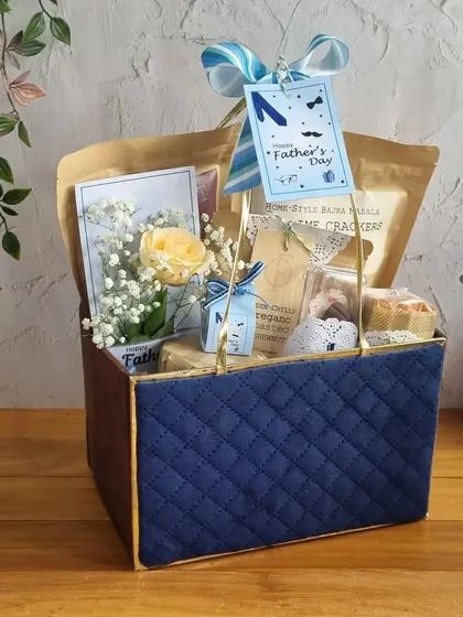 A quilted blue gift box for Father's Day, filled with snacks and a single yellow rose for a touch of sunshine.