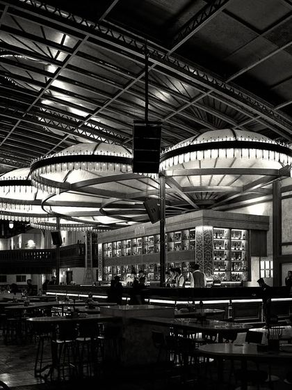 This grayscale image focuses on the powerful silhouettes of the bar and lighting. It strips away color to reveal the fundamental architectural shapes and the interplay of light and shadow.
