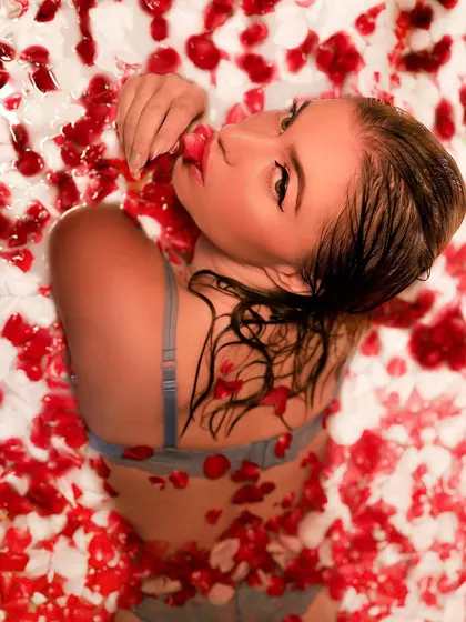 An artistic overhead shot of a model in a milk bath filled with red and white rose petals, creating a visually stunning and romantic image. This is a popular creative concept I offer.