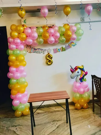 An 8th birthday party with a unicorn theme. This home setup includes a colorful L-shaped balloon arch and a unicorn balloon column, creating a festive corner for the celebration.