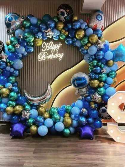 For a 9th birthday, I designed this outer space adventure theme. The square balloon arch is filled with metallic blue, gold, and silver balloons, along with astronaut, moon, and star-shaped foils, all centered around a 'Happy Birthday' neon sign.