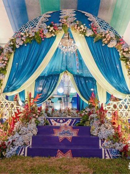 A stunning turquoise and blue themed mandap for a mehendi ceremony. The dome-shaped structure is adorned with intricate lattice work and floral arrangements, creating a grand and elegant look.