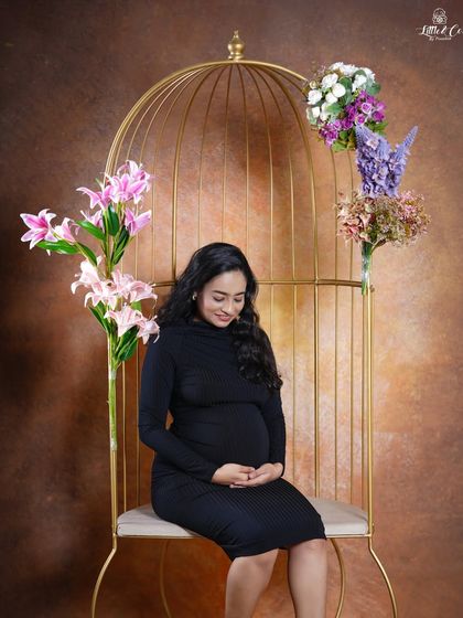 A serene solo shot of the expectant mother seated on the golden birdcage chair. Her gentle smile and the way she cradles her bump create a peaceful and loving portrait.