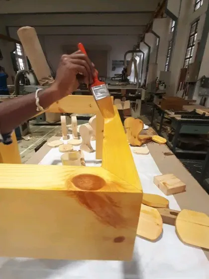 A student carefully applies a coat of finish with a brush, bringing out the natural color and grain of the pinewood.