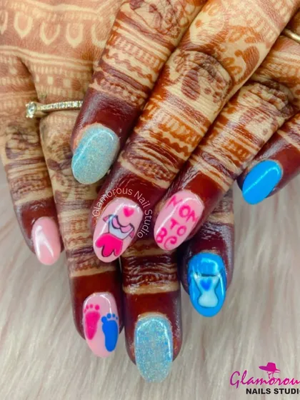 The cutest "Mom to Be" nails for a special celebration. We combined glittery blue and soft pink nails with custom hand-painted art, including baby clothes, footprints, and an hourglass, all set against the client's beautiful mehndi.