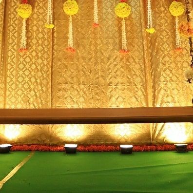 The complete stage setup for a traditional ceremony. A wooden swing, or 'oonjal', is placed before the ornate backdrop, with uplighting highlighting the rich textures of the fabric and flowers.