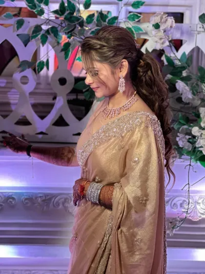 A candid shot of a client in a beautiful golden saree, ready for an evening function. Her makeup is soft and glowing, with a stylish ponytail.