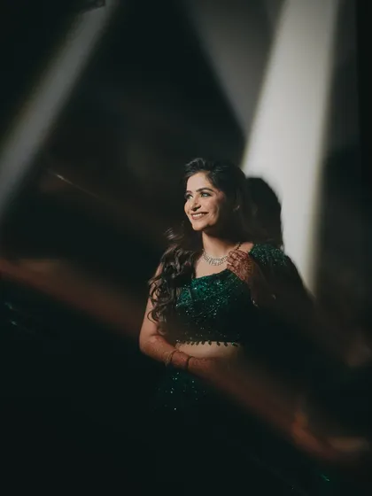 A candid bridal portrait captured through a creative foreground. The out-of-focus elements add depth and an artistic touch, drawing the eye to her joyful, smiling expression.