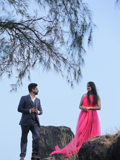 A beautifully composed pre-wedding photo, with the couple framed by a tree branch. The pink trail gown adds a touch of romance to the natural setting.