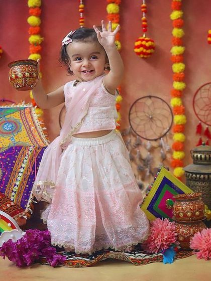 Eid Mubarak! This little girl looks so precious in her traditional lehenga, waving happily in a festive setup with marigolds and lanterns.