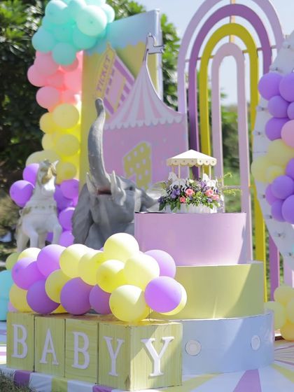 A close-up of the carnival cake stage, featuring a tiered cake stand and an elephant prop surrounded by pastel balloons. The details create a sweet and celebratory focal point.