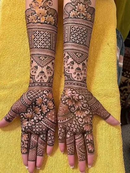 This full bridal mehndi showcases a variety of techniques, from delicate floral work to intricate net patterns. The design also features hanging jhumkas and lotus motifs for a festive feel.