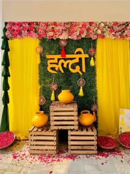 A lovely Haldi backdrop with a green panel, wooden crates for props, and bowls of flower petals. This setup is perfect for home-based functions and provides great photo opportunities.