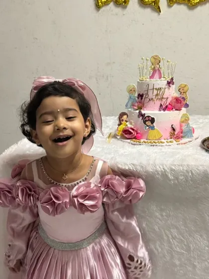 The birthday princess with her big, happy smile, standing proudly next to her two-tier princess cake. These are the memories that last a lifetime.