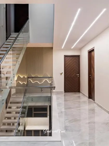 A modern staircase with a glass balustrade and floating wooden steps. The geometric wall paneling and linear ceiling lights add a dynamic and architectural quality to the space.