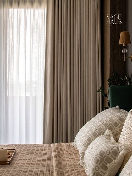 A close-up on the layered bedding and curtains. The mix of textures, from the patterned pillows to the crisp linen, adds depth and interest to the neutral color scheme.