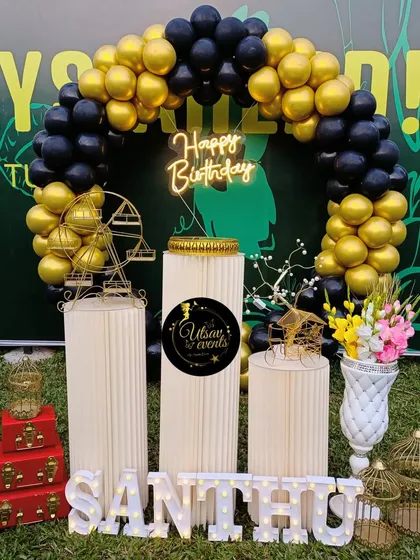 An outdoor birthday setup with a black and gold balloon arch. This decor looks great against the green background of a lawn.