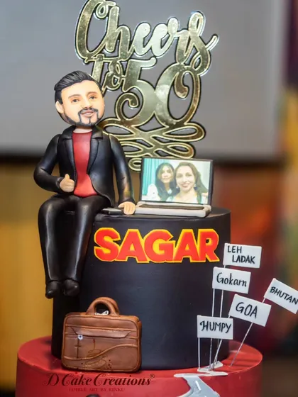 A detailed shot of the topper for Sagar's 50th birthday cake, showing a custom figurine, a laptop with a family photo, and signs of his favorite biking routes like Leh and Ladakh.