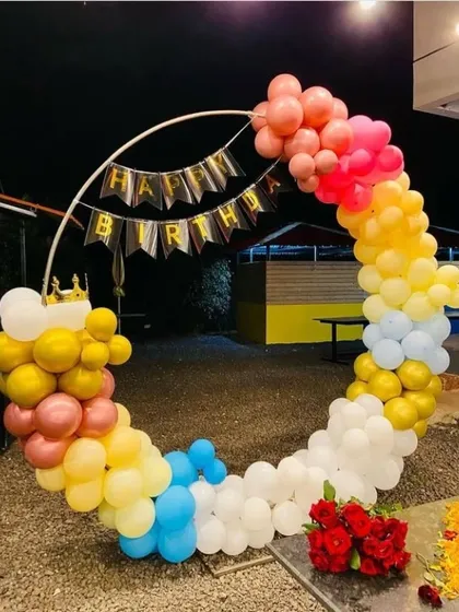 A colorful circular balloon arch for an outdoor birthday party. The mix of pastel and bright colors, along with a 'Happy Birthday' banner, creates a festive and joyful look.