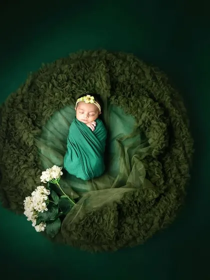 A beautiful overhead shot of a newborn wrapped in green, nestled in a soft, mossy bed. This creates a lovely, nature-inspired "nest" effect.