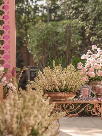 A beautiful decor vignette with pink florals and traditional elements set against a carved pink jaali screen.