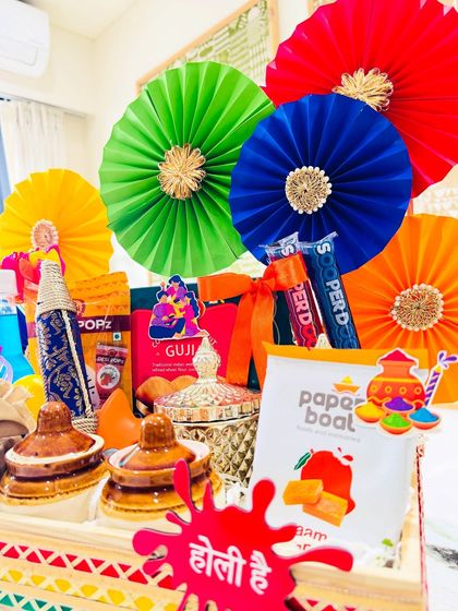 This image captures the vibrant energy of the traditional Holi hamper. The bright red, green, blue, and yellow pinwheels contrast beautifully with the earthy tones of the jars, creating a gift that is both luxurious and full of festive spirit.