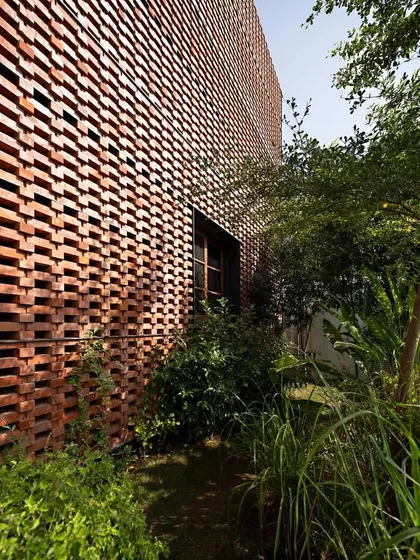 The perforated brick wall of the Ishtika house acts as a screen for a private garden path. We planted a mix of trees and shrubs that thrive in the filtered light, creating a cool and shaded walkway.