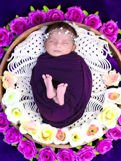 This overhead shot shows a newborn peacefully sleeping in a basket, encircled by beautiful purple and white roses. We use floral arrangements to add a touch of natural beauty.