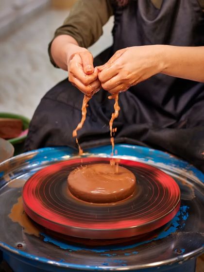 The wet clay drips through the artist's hands as she prepares the wheel. This sensory detail is a core part of the tactile experience of wheel-thrown pottery.