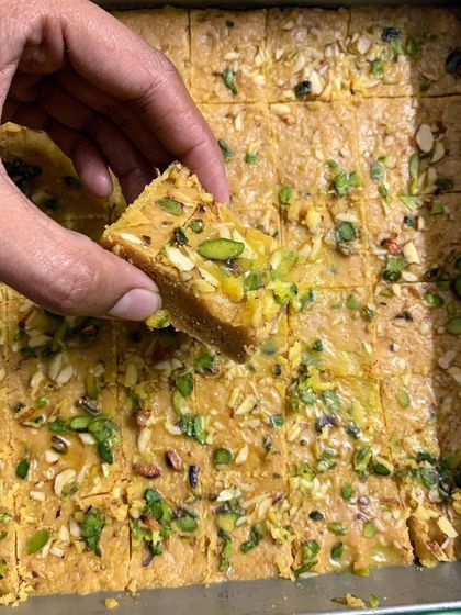 A hand picking up a piece of my freshly made Mohanthal, a rich and nutty gluten-free sweet. It's a melt-in-your-mouth delicacy perfect for gifting.