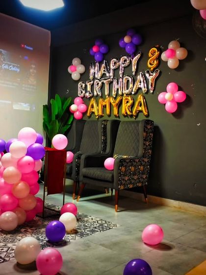 A birthday setup for Amyra's 8th birthday in a private party room. The decor features pink, purple, and white balloons and a foil letter banner.