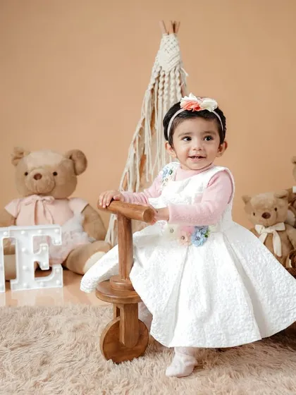 This first birthday setup features a soft, neutral palette with a macrame teepee, teddy bears, and a light-up "ONE" sign for a cozy and modern feel.