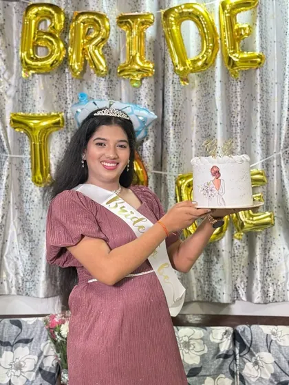 The happy bride-to-be posing with her custom cake at her party, surrounded by "BRIDE TO BE" balloons.