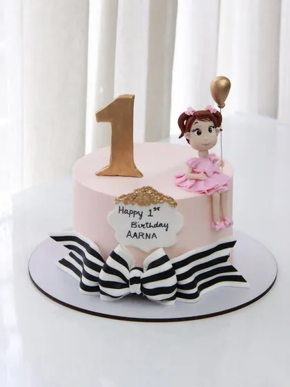 A chic and sweet 1st birthday cake for Aarna, featuring a stylish black and white striped bow and a cute girl topper.