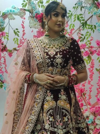 A bride wearing a deep maroon velvet lehenga with intricate floral embroidery. The peach-colored dupatta adds a beautiful contrast.