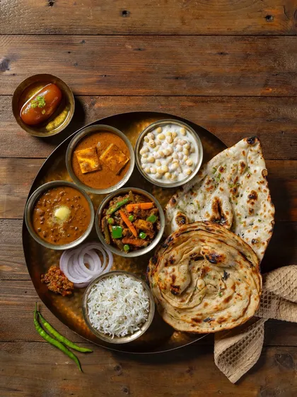 A traditional vegetarian thali, shot for Grover Sweets. This top-down photograph is styled to present a complete, balanced meal, showcasing a variety of North Indian dishes like shahi paneer, dal makhani, and assorted breads for their menu.