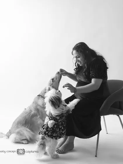 A candid, black and white moment from a maternity session with pets. The mom-to-be shares a treat with her dogs, creating a natural and loving interaction that tells a beautiful story.