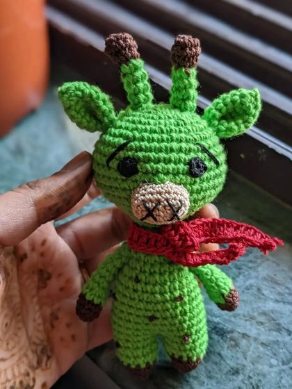 A vibrant green giraffe with a red scarf, held in my hand.
