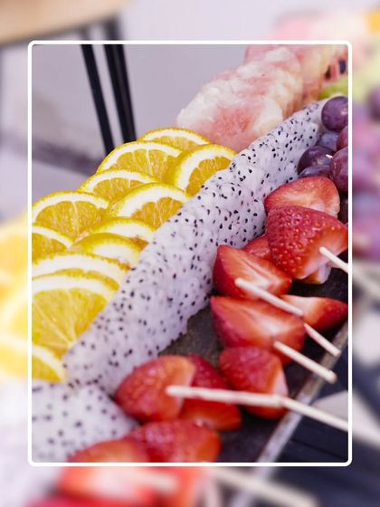 A vibrant display of fresh fruit skewers, including orange slices, dragon fruit, strawberries, and grapes. A healthy, colorful, and refreshing option for any event.