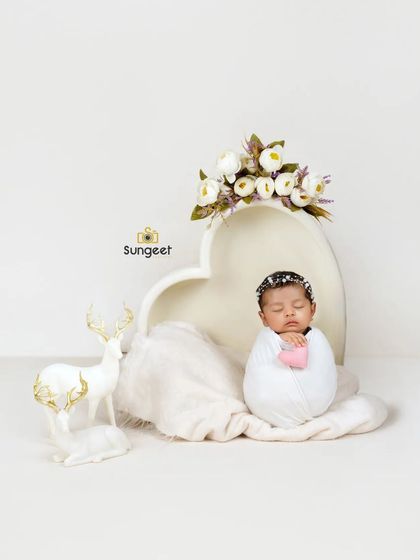 Pure and simple elegance. A newborn swaddled in white rests peacefully in a heart-shaped bowl, accented with white flowers and a deer figurine for a touch of woodland magic.